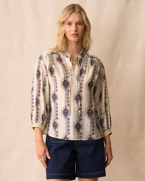 Neris model wearing a patterned blouse and navy shorts against a beige background