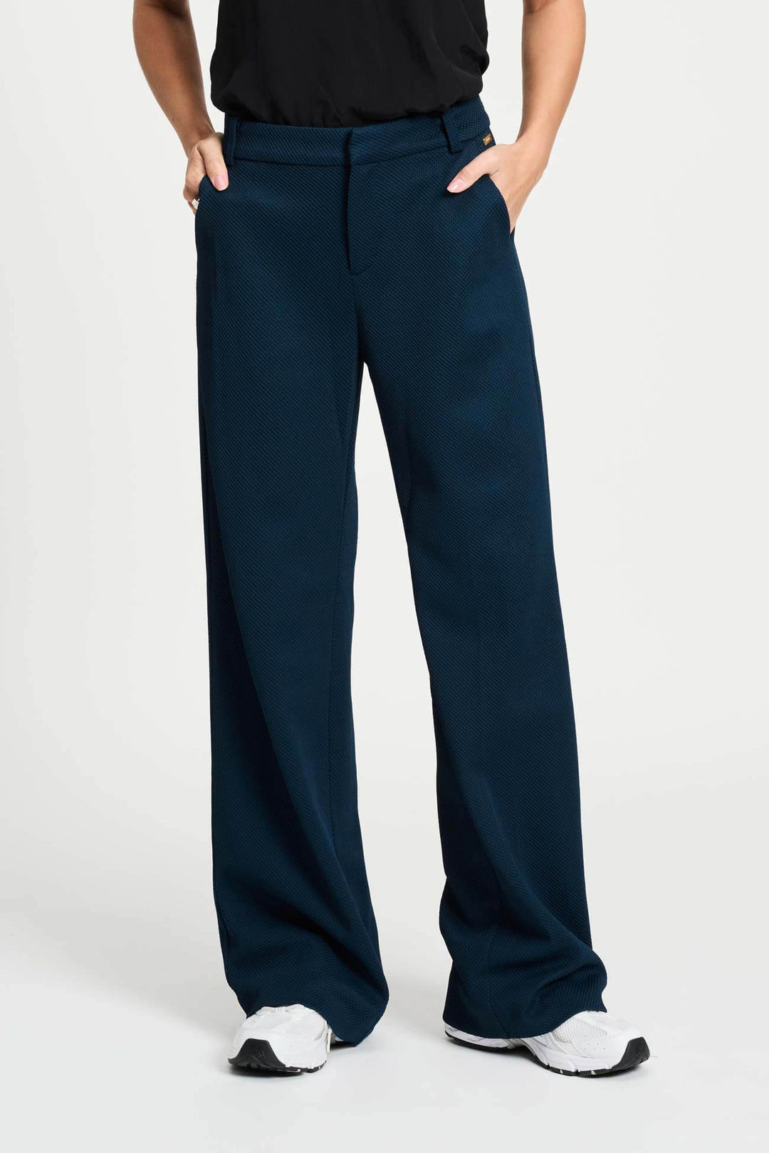 Pom Amsterdam model wearing navy blue wide-leg trousers with a blacktop partially visible, photographed against a clean white studio background.