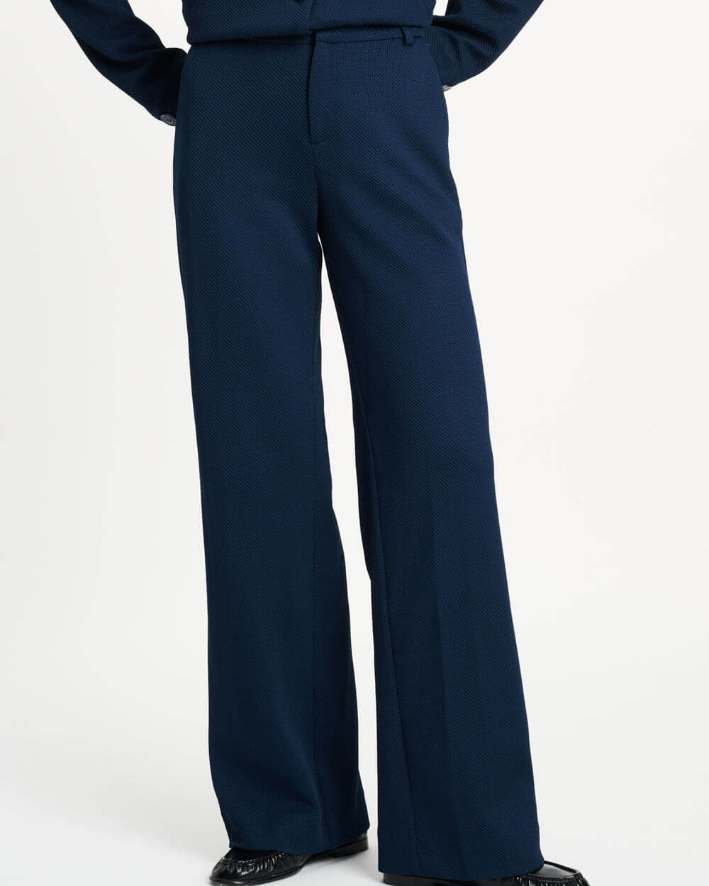 Pom Amsterdam model wearing navy blue wide-leg trousers with a matching top partially visible, photographed against a clean white studio background.