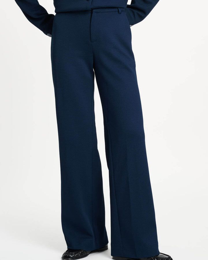 Pom Amsterdam model wearing navy blue wide-leg trousers with a matching top partially visible, photographed against a clean white studio background.