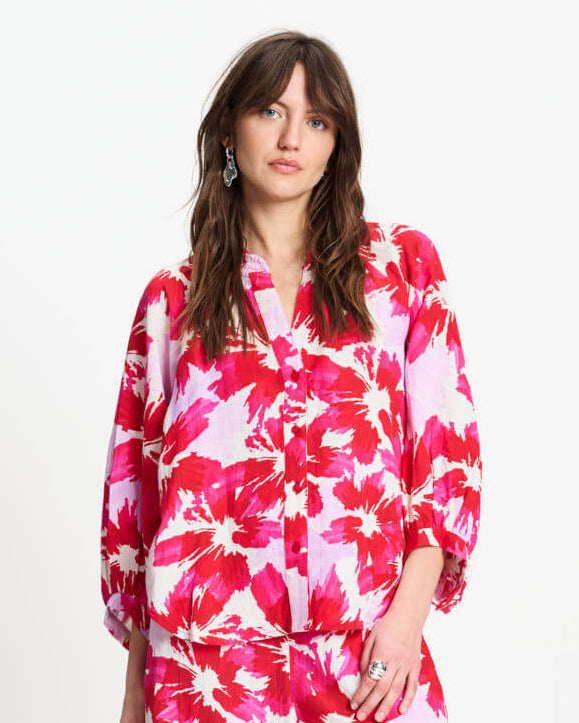 Pom Amsterdam  woman modeling a matching two-piece pajama set with a bold pink, red, and white floral print, standing against a plain white studio background.