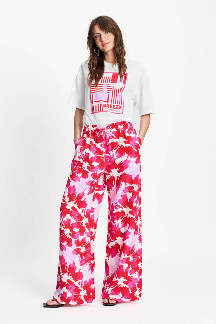 Woman wearing a white t-shirt with red graphics and pink floral pants on a white background