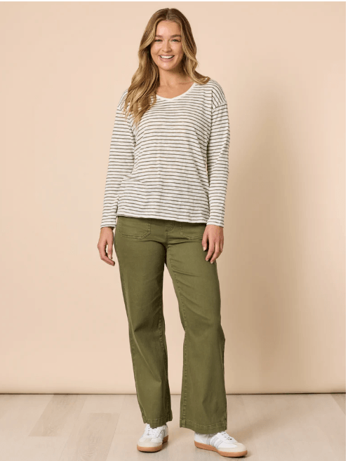 Threadz model  wearing olive green wide-leg pants, a white and beige striped long-sleeve top, and white sneakers with red stripes, standing against a plain beige studio background.