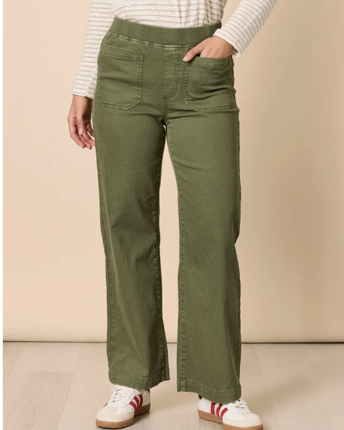 Threadz model  wearing olive green wide-leg pants, a white and beige striped long-sleeve top, and white sneakers with red stripes, standing against a plain beige studio background.