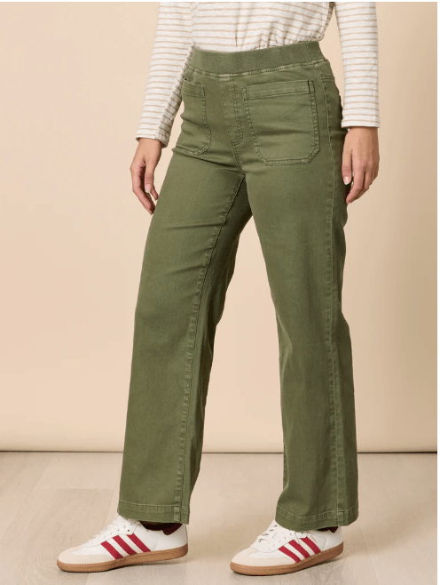 Threadz model  wearing olive green wide-leg pants, a white and beige striped long-sleeve top, and white sneakers with red stripes, standing against a plain beige studio background.