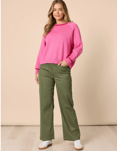 Threadz woman  modeling a bright pink crewneck sweater and olive green wide-leg pants against a solid beige studio background.