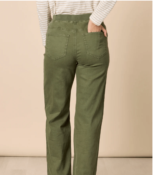 Threadz model  wearing olive green wide-leg pants, a white and beige striped long-sleeve top, and white sneakers with red stripes, standing against a plain beige studio background. Showing the back view.
