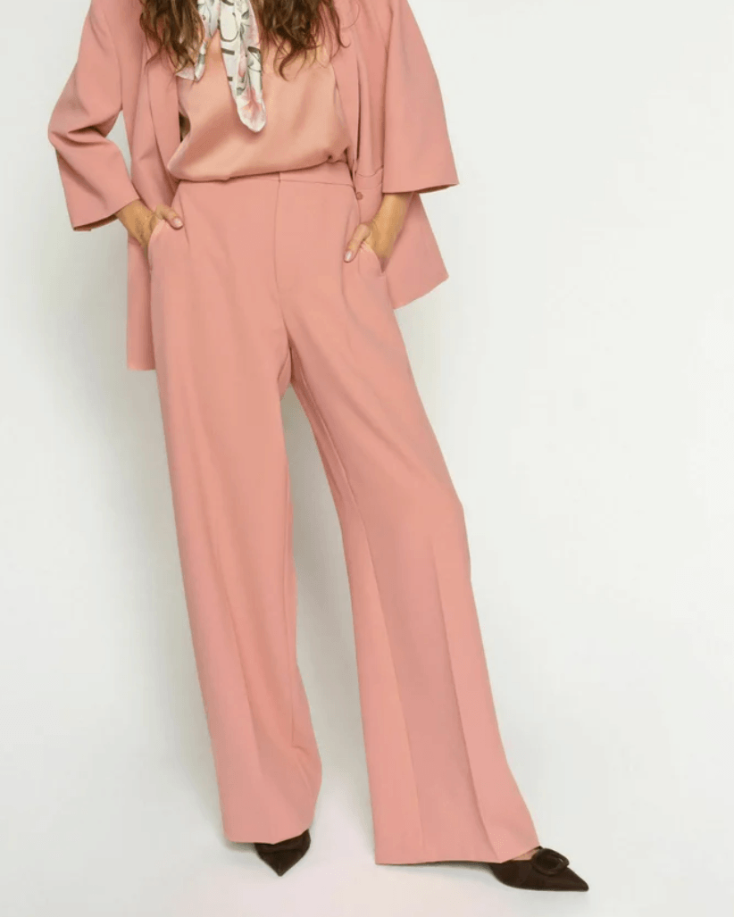 Mos Mosh A woman modeling a dusty pink two-piece suit consisting of a long-sleeve blazer and matching wide-leg trousers, styled with a patterned neck scarf and dark brown pointed-toe flats against a plain white studio background.