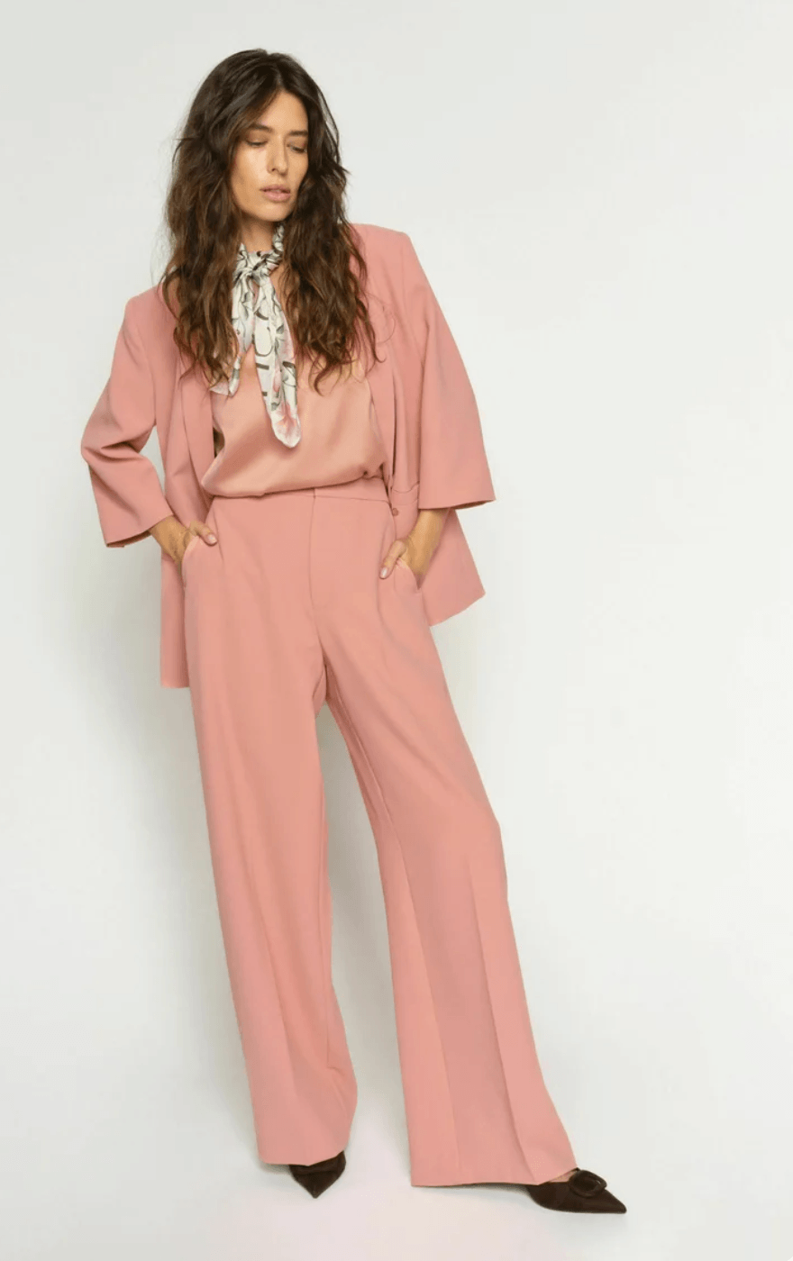 Mos Mosh A woman modeling a dusty pink two-piece suit consisting of a long-sleeve blazer and matching wide-leg trousers, styled with a patterned neck scarf and dark brown pointed-toe flats against a plain white studio background.