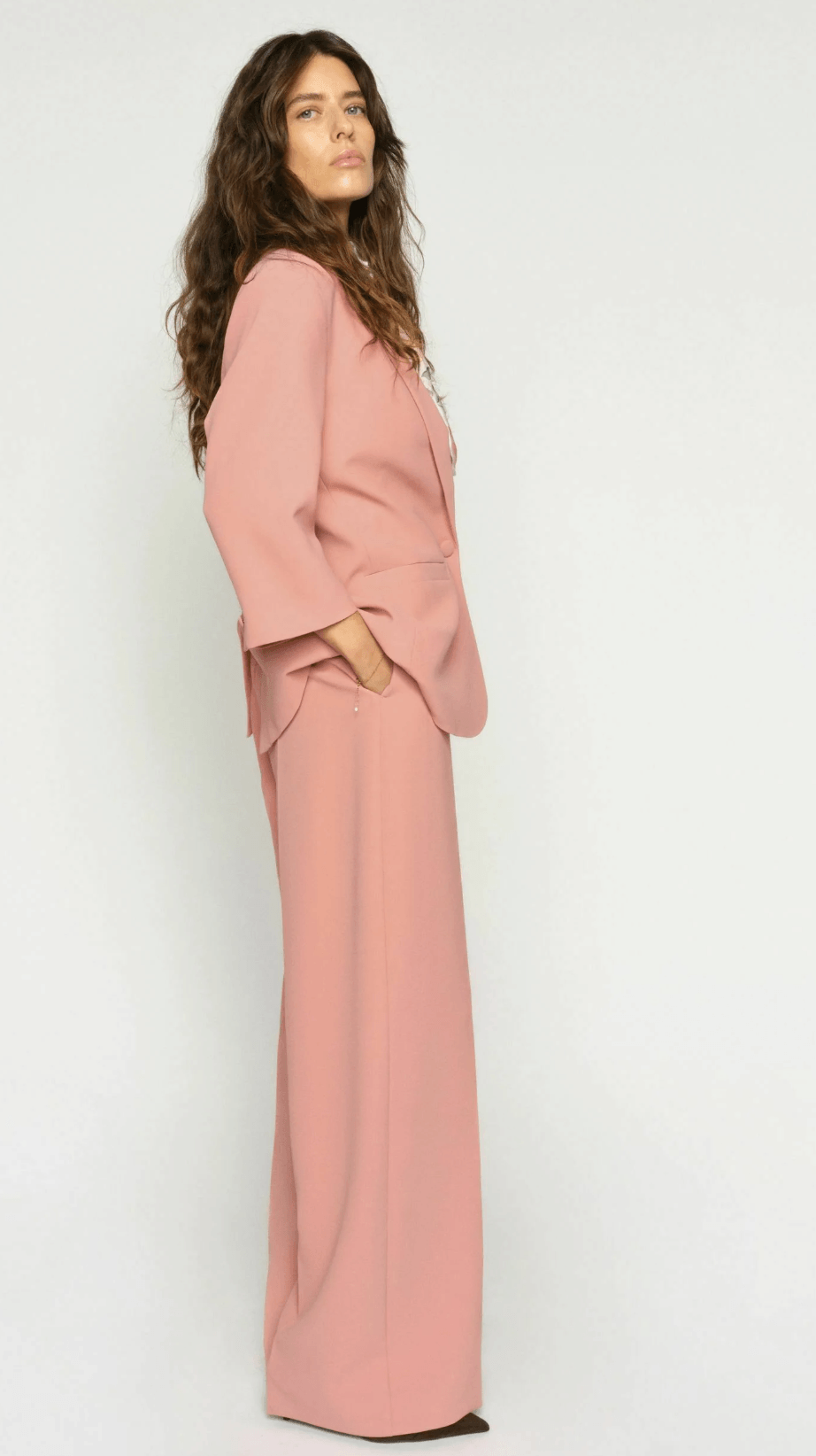 Mos Mosh A woman modeling a dusty pink two-piece suit consisting of a long-sleeve blazer and matching wide-leg trousers, styled with a patterned neck scarf and dark brown pointed-toe flats against a plain white studio background.