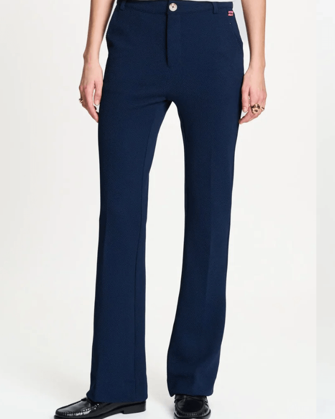 Pom Amsterdam  model wearing a pair of dark navy blue straight-leg trousers, styled with a white graphic t-shirt and black loafers, against a plain white studio background.