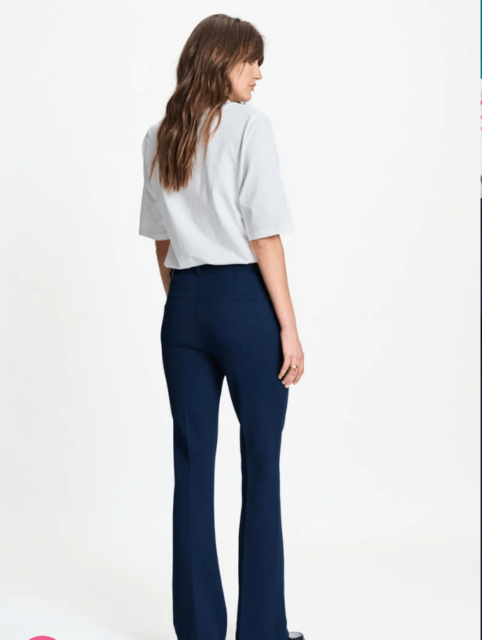Pom Amsterdam  model wearing a pair of dark navy blue straight-leg trousers, styled with a white graphic t-shirt and black loafers, against a plain white studio background. Back view.