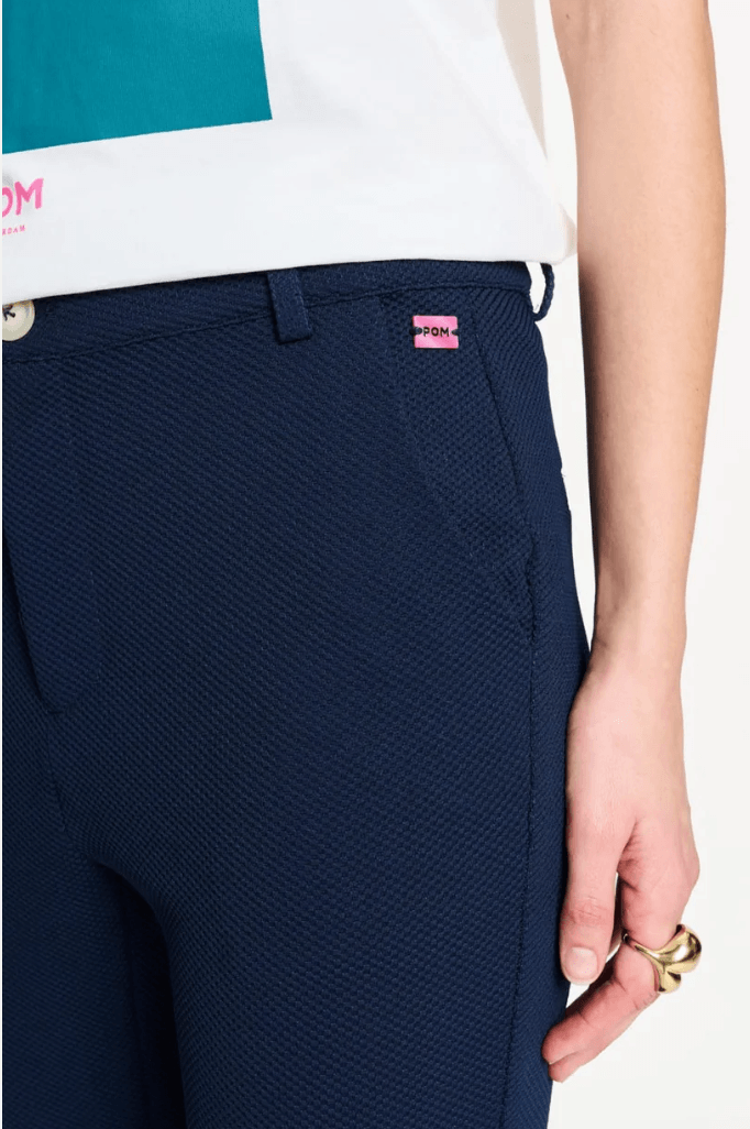 Pom Amsterdam  model wearing a pair of dark navy blue straight-leg trousers, styled with a white graphic t-shirt and black loafers, against a plain white studio background. Close up.