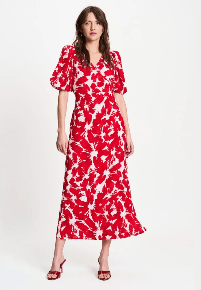 Pom Amsterdam  modeling a red and white abstract floral print midi dress with puff sleeves and a V-neckline, paired with red heeled sandals against a plain white studio background.