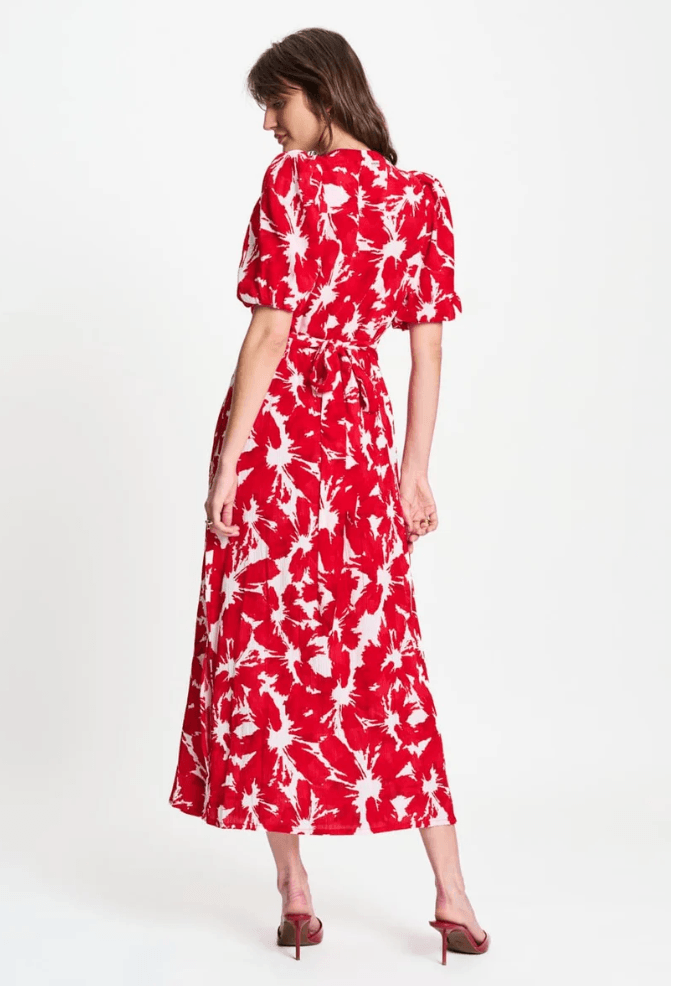 Pom Amsterdam  modeling a red and white abstract floral print midi dress with puff sleeves and a V-neckline, paired with red heeled sandals against a plain white studio background. Back view.
