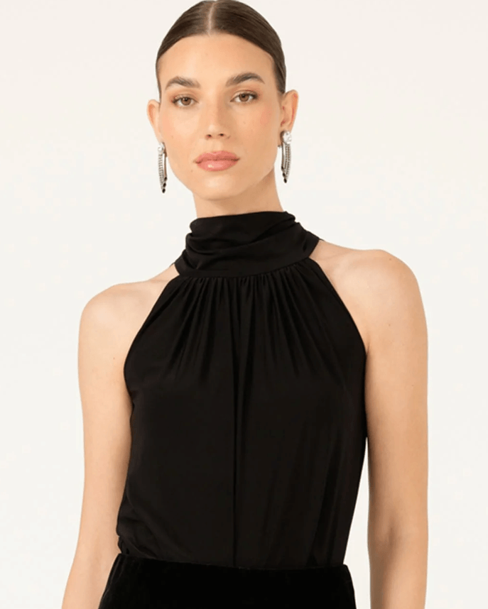 Sacha Drake modeling a black halter-neck top with a gathered, pleated high neckline, shown against a plain light background.