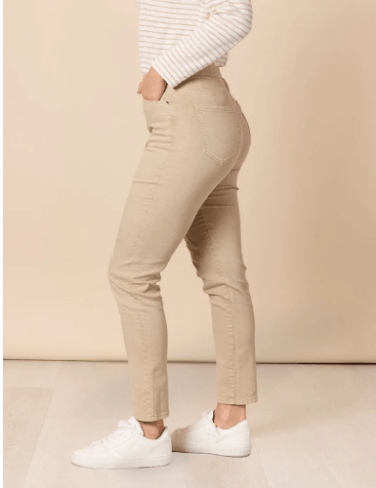 Threadz model  wearing beige slim-fit jeans with distressed details on the thighs, paired with a white and beige striped long-sleeve top and white sneakers, standing against a solid beige background.