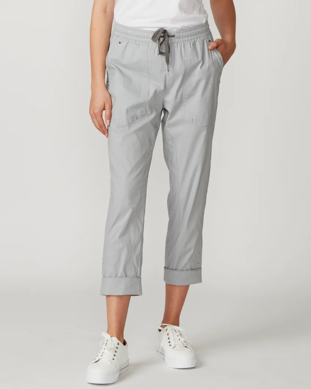Lania The Label  light gray cropped pants with an elastic drawstring waist and rolled cuffs, paired with a white top and white sneakers, photographed against a plain light gray studio background.