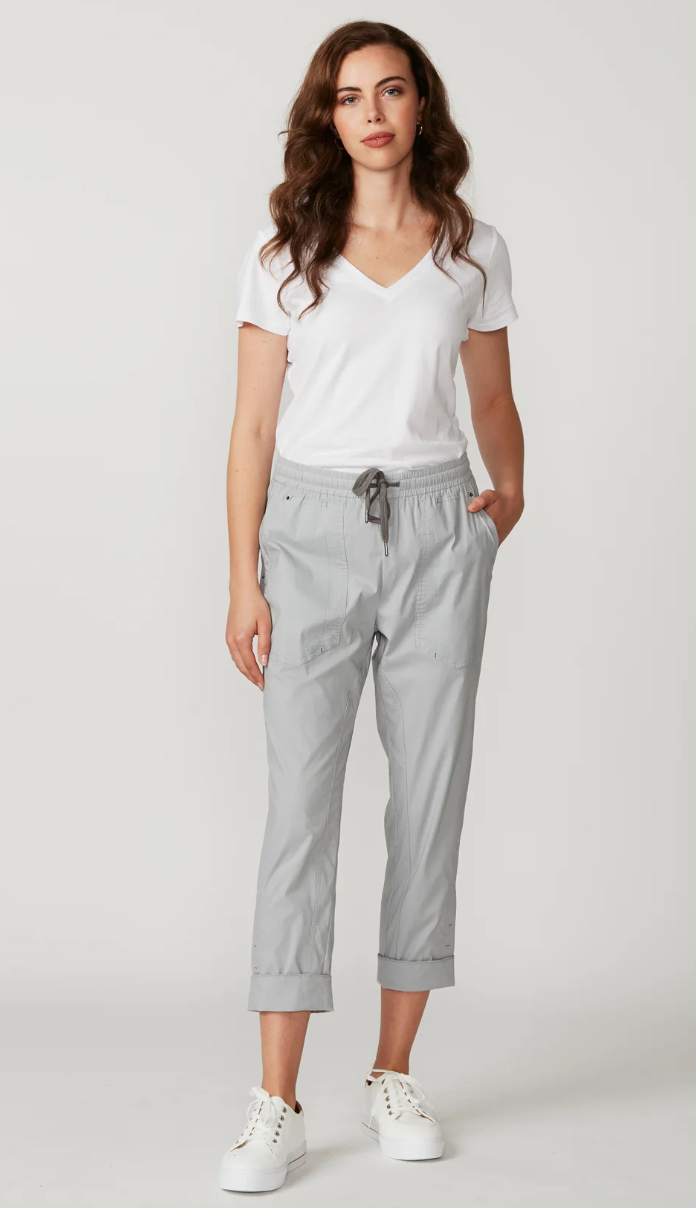 Lania The Label  light gray cropped pants with an elastic drawstring waist and rolled cuffs, paired with a white top and white sneakers, photographed against a plain light gray studio background.