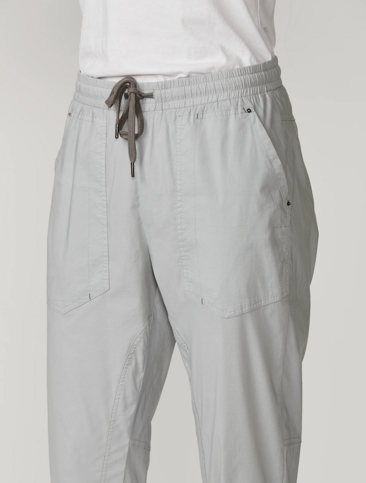 Lania The Label  light gray cropped pants with an elastic drawstring waist and rolled cuffs, paired with a white top and white sneakers, photographed against a plain light gray studio background.