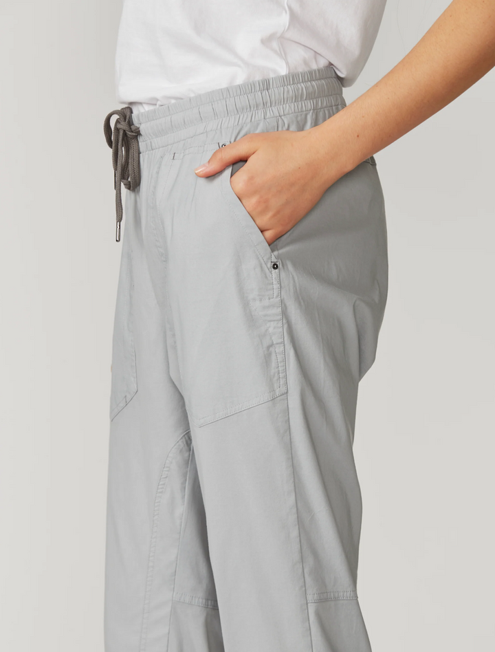 Lania The Label  light gray cropped pants with an elastic drawstring waist and rolled cuffs, paired with a white top and white sneakers, photographed against a plain light gray studio background.