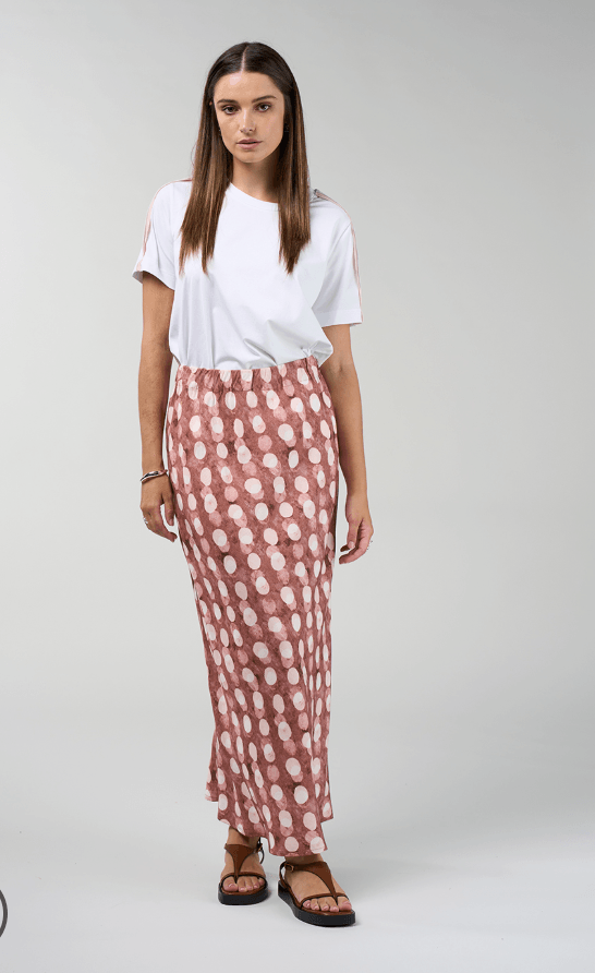 Madly Sweetly model in a pink midi skirt with allover white dot print and elastic gathered waist. On a studio background-pink midi skirt with scattered white polka dots and elastic waist