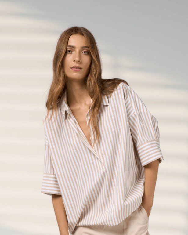 Madly Sweetly model  wearing light beige drawstring cropped pants with a striped shirt and brown sandals, standing against a light gray studio background with soft window-like shadows.