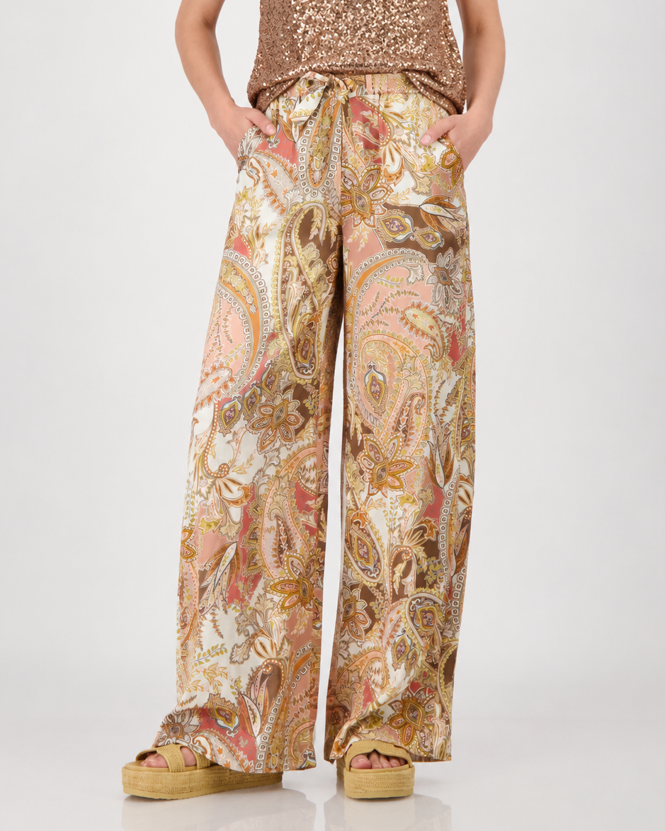 Monari model is shown from the waist down wearing wide-leg trousers with a detailed paisley pattern in shades of beige, brown, pink, and gold. The pants feature an elastic drawstring waist and side pockets, paired with platform sandals on a light gray studio background.