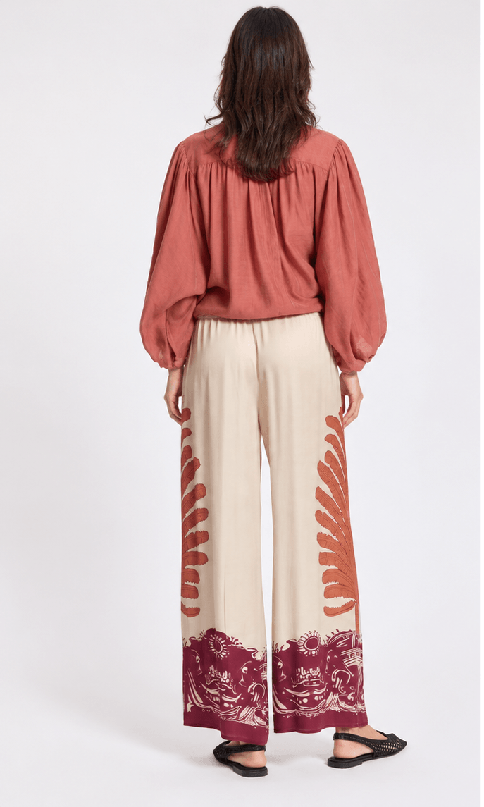 Cream 7/8 pants with rust-red abstract side print and burgundy hem border, wide leg